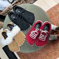 Three pairs of toe shoes displayed on a round table - black athletic toe shoes, red lace-up toe shoes, and brown sandals with white fur straps