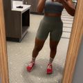 Woman taking mirror selfie in gym locker room wearing athletic wear and red sneakers