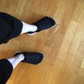 Person wearing black quilted slippers with white socks standing on a wooden floor, viewed from above.