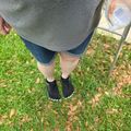 Person standing on grass wearing dark shoes and holding a ladder