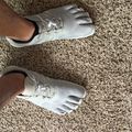 Person wearing silver athletic shoes with toe-like compartments standing on textured carpet