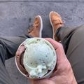 A person holding an ice cream cone with two scoops - one vanilla with purple speckles and one chocolate - against a concrete background, with their tan and white sneakers visible in the background.