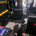 Person wearing black haptic gloves sitting in a garage workshop with VR equipment and various tools and storage items visible