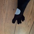 A person wearing a black glove with white stitching detail on the back, standing on wooden flooring