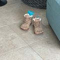 A pair of tan hiking boots with white fleece lining sitting on a tiled floor next to outdoor furniture