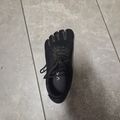 A single black toe shoe with individual toe compartments and laces sitting on a tiled floor