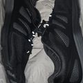 A pair of black athletic sneakers with mesh panels and white laces, displayed in a white box with tissue paper.