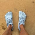 Overhead view of a person wearing light blue five-fingered toe shoes standing on a tan concrete surface.