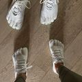 Two pairs of feet wearing white toe shoes with individual compartments for each toe, standing on a wooden floor