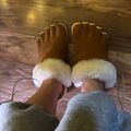 Person wearing brown toe-separated slippers with white fur trim while sitting on wooden floor