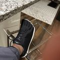 Person wearing black sneakers with feet resting in clear acrylic footrest under granite kitchen counter