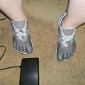 Person wearing gray toe shoes with individual toe compartments standing on carpet next to a black electronic device