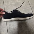 A black sneaker with white sole being held by a hand on a tiled floor