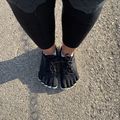 Overhead view of a person wearing black leggings and black five-toe running shoes standing on a concrete surface with a white line running between their feet.
