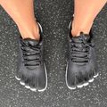 Person wearing black toe shoes with individual toe compartments standing on asphalt pavement