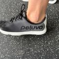 Person wearing black and white mesh athletic sneakers standing on speckled pavement