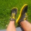 Person wearing black and yellow athletic shoes with toe compartments sitting on grass