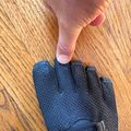 A hand wearing a black textured glove with velcro straps on a wooden floor surface