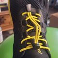 Black athletic shoe with yellow laces and accents being worn on someone's foot