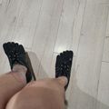 Person wearing black five-finger toe shoes standing on light gray wooden flooring, viewed from above.
