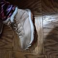 A beige hiking boot with laces and fuzzy lining sits on a wooden parquet floor