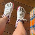 Person wearing white and pink toe shoes with individual toe compartments, standing on wooden deck boards