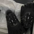 Black athletic shoes with toe compartments and lacing system displayed in white tissue paper packaging
