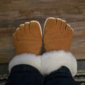 A pair of brown leather gloves with white fur trim worn on hands, photographed against a wooden background