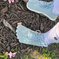 Person wearing light blue mesh athletic shoes with white soles standing on mulch ground with pink flowers and green plants nearby