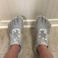 Person wearing gray toe shoes with individual toe compartments, standing on tiled floor