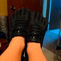 Person wearing black fingerless gloves with individual toe sections, sitting indoors