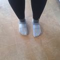 Person wearing black leggings and gray toe shoes with individual toe compartments standing on tiled floor