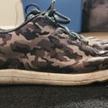 A camouflage patterned sneaker with laces sitting on a dark surface