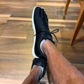 Person wearing black athletic shoes with white soles sitting on wooden floor