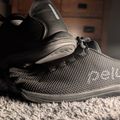 A pair of gray athletic sneakers with black laces sitting on a textured carpet in an indoor setting
