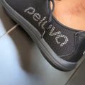 A person's foot wearing a dark gray slip-on shoe with mesh material and decorative rhinestone detailing on the side, displayed against a light background.