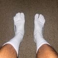 Pair of white crew socks with toe separation design worn on feet, photographed from above on a beige carpet.