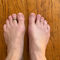 A pair of bare feet on a wooden floor, with small rings on two toes
