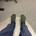 Person wearing quilted slippers with individual toe sections, sitting with feet up on a footrest in an office setting with carpeted floor