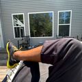 Person relaxing on a wooden deck outside a house, wearing yellow sneakers with legs stretched out