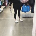 Person shopping in clothing store wearing black outfit and white sneakers, holding blue shopping bag