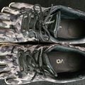A pair of camouflage patterned athletic shoes with black laces and soles, placed on a dark surface