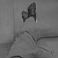 Black and white overhead view of a person wearing black lace-up boots with white soles, sitting on a concrete surface with legs extended upward.