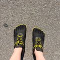 Person wearing black toe shoes with yellow laces standing on asphalt pavement