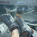 Person wearing white sneakers with feet up on car dashboard, view through windshield showing storefronts including a salon