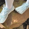 Person wearing light blue athletic shoes with white socks standing on a large flat rock outdoors