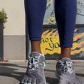 A person wearing navy blue textured leggings and gray and mint green five-fingered running shoes stands on a sidewalk in front of a storefront with flame graphics and yellow signage.