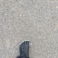 Person wearing black toe shoes standing on gray asphalt pavement