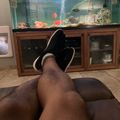 Person relaxing on a couch with feet up, viewing a large aquarium with colorful fish and coral decorations in a living room setting.