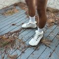 A person wearing white sneakers and white socks stands on a blue wooden deck scattered with dried palm fronds and plant debris.